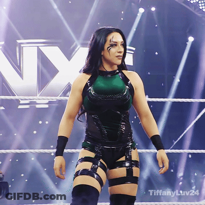 A Woman In A Green And Black Outfit Is Standing In A Wrestling Ring With Tiffanyluv24 Written On The Bottom GIF