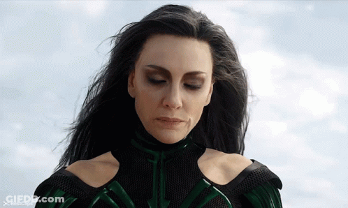 A Woman In A Green And Black Superhero Costume Is Looking Down At Something GIF