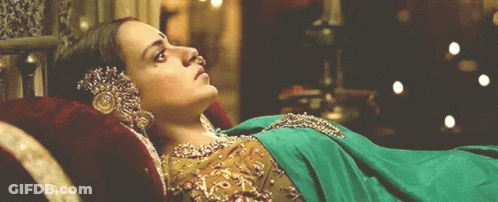A Woman In A Green And Gold Dress Is Laying Down GIF