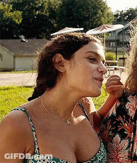A Woman In A Green And White Floral Tank Top Looks Down At Something GIF