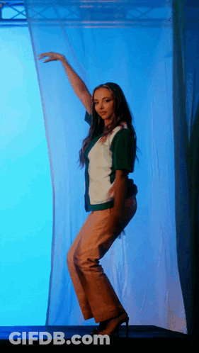 A Woman In A Green And White Shirt Is Dancing In Front Of A Blue Background GIF