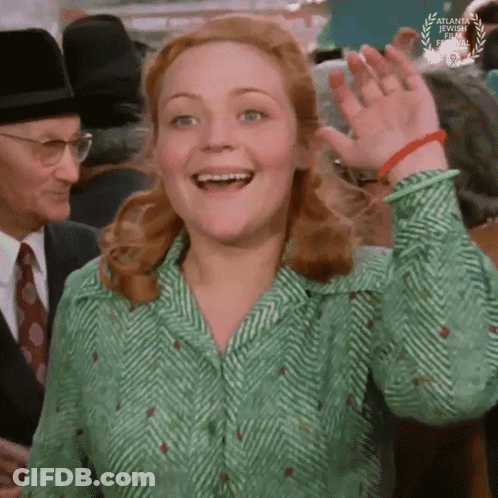 A Woman In A Green And White Shirt Is Smiling And Waving GIF