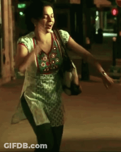 A Woman In A Green And White Top Is Dancing On A Street At Night GIF