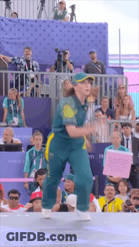 A Woman In A Green And Yellow Outfit Is Dancing In Front Of A Crowd Of People GIF