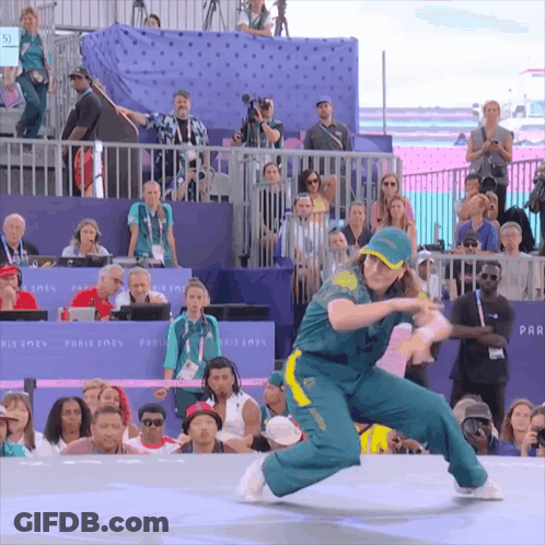 A Woman In A Green And Yellow Outfit Is Dancing In Front Of A Crowd That Is Watching GIF