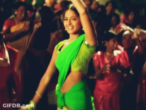A Woman In A Green And Yellow Saree Is Dancing In A Crowd GIF