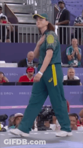A Woman In A Green And Yellow Uniform Is Walking In Front Of A Crowd . GIF