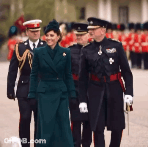 A Woman In A Green Coat Is Walking With A Group Of Men In Uniforms GIF