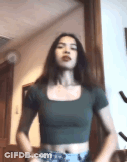 A Woman In A Green Crop Top And Shorts Is Standing In A Room . GIF
