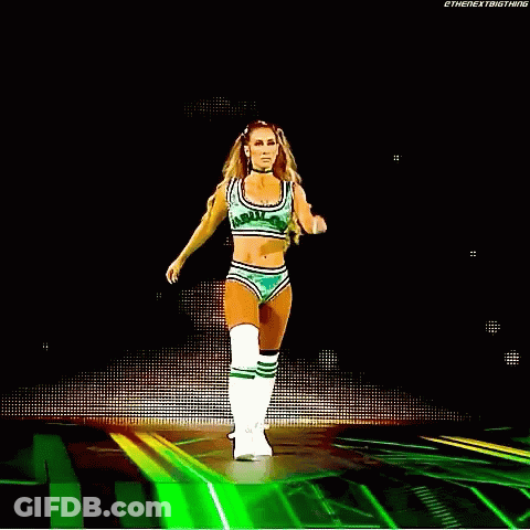 A Woman In A Green Crop Top And Shorts Is Walking On A Stage . GIF