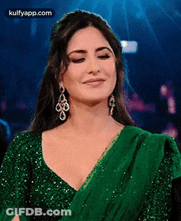 A Woman In A Green Dress And Earrings Is Smiling . GIF