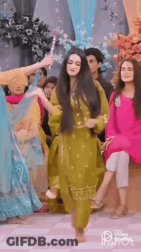 A Woman In A Green Dress Is Dancing Barefoot In Front Of A Group Of People . GIF
