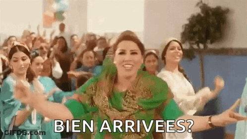 A Woman In A Green Dress Is Dancing In Front Of A Crowd With The Words Bien Arrivees ? Written Below Her . GIF