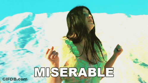 A Woman In A Green Dress Is Dancing In Front Of A Snowy Mountain And The Word Miserable Is Written Below Her GIF