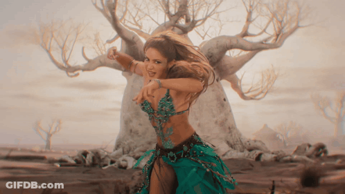 A Woman In A Green Dress Is Dancing In Front Of A Tree In The Desert GIF