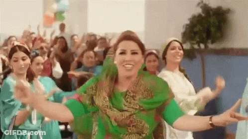 A Woman In A Green Dress Is Dancing With A Group Of Women In Blue Dresses . GIF