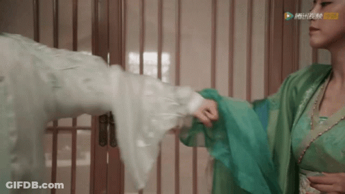 A Woman In A Green Dress Is Holding A Man 'S Arm In A Room GIF