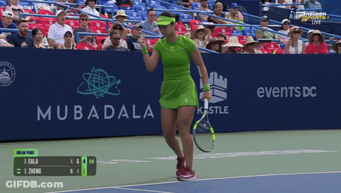 A Woman In A Green Dress Is Holding A Tennis Racquet In Front Of A Mubadala Advertisement GIF