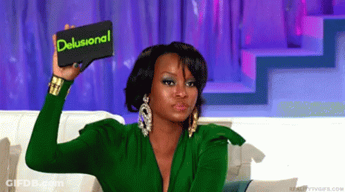 A Woman In A Green Dress Is Holding Up A Card That Says Delusional GIF