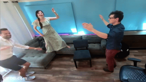 A Woman In A Green Dress Is Jumping In The Air While Two Men Watch GIF