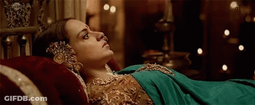 A Woman In A Green Dress Is Laying On A Bed With A Red Pillow . GIF