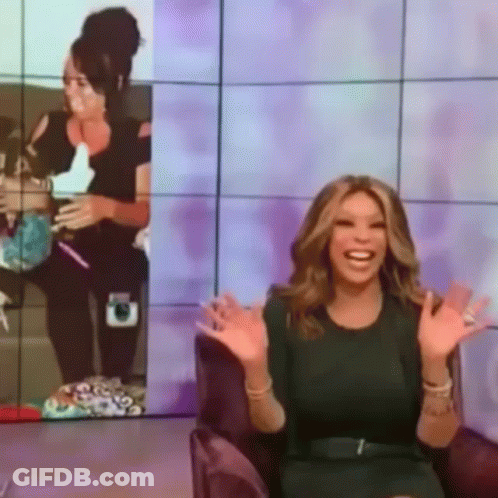 A Woman In A Green Dress Is Sitting In Front Of A Purple Wall GIF