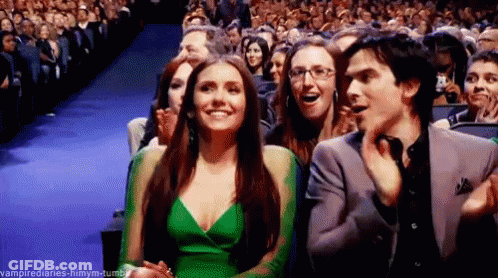 A Woman In A Green Dress Is Sitting Next To A Man In A Suit In Front Of A Crowd . GIF