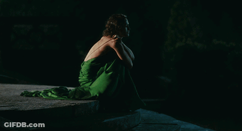 A Woman In A Green Dress Is Sitting On A Rock In The Dark GIF