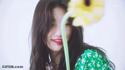 A Woman In A Green Dress Is Smiling While Holding A Yellow Flower In Front Of Her Face GIF