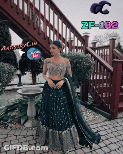 A Woman In A Green Dress Is Standing In Front Of A Staircase With Artistryc.in Written On The Bottom GIF