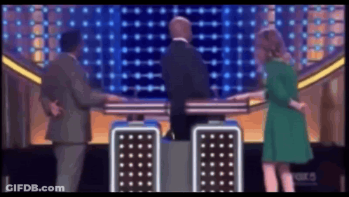 A Woman In A Green Dress Is Standing Next To A Man In A Suit GIF