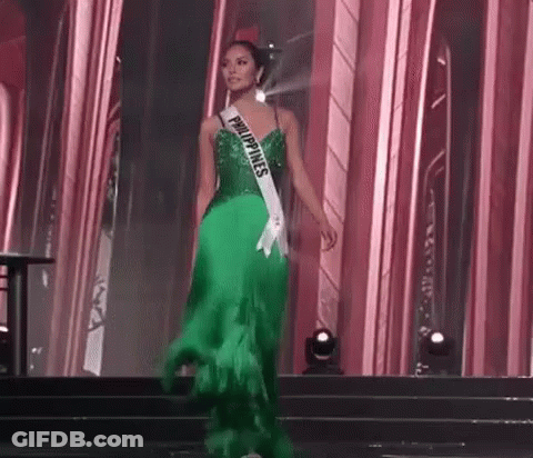A Woman In A Green Dress Is Walking Down A Stage At A Pageant . GIF