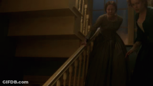 A Woman In A Green Dress Is Walking Down A Staircase GIF