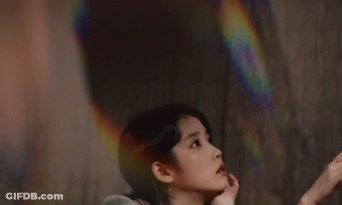 A Woman In A Green Dress Reaches For A Pink Rose GIF