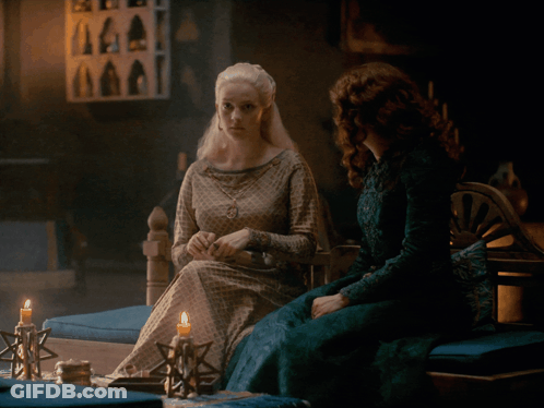 A Woman In A Green Dress Sits Next To A Woman In A White Dress GIF