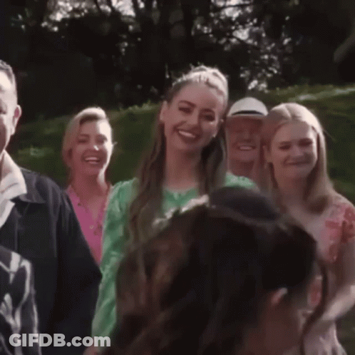 A Woman In A Green Dress Smiles While Standing In A Crowd Of People GIF