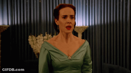 A Woman In A Green Dress Stands In Front Of A Curtain GIF