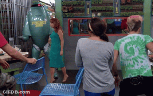 A Woman In A Green Dress Stands In Front Of A Green Robot That Says Zugrut GIF