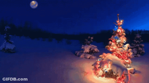 A Woman In A Green Dress Stands In Front Of A Snowy Christmas Tree GIF
