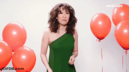 A Woman In A Green Dress Stands In Front Of Red Balloons With Marieclaire Written On The Bottom Right GIF