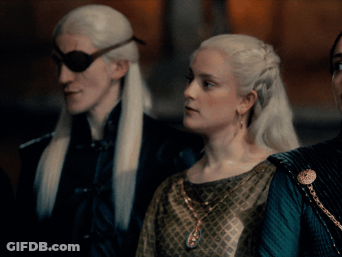 A Woman In A Green Dress Stands Next To A Man In A Black Jacket GIF