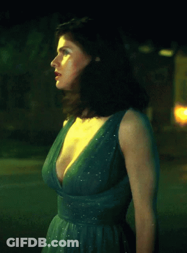 A Woman In A Green Dress With A Plunging Neckline Is Standing In Front Of A Yellow Sign GIF