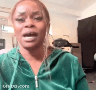 A Woman In A Green Hoodie Is Making A Funny Face While Standing In A Room . GIF