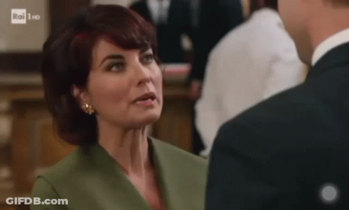 A Woman In A Green Jacket And Earrings Is Talking To A Man In A Suit . GIF