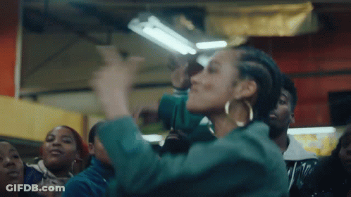 A Woman In A Green Jacket Is Dancing In Front Of A Crowd . GIF