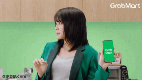 A Woman In A Green Jacket Is Holding A Cell Phone That Says Grab Mart GIF