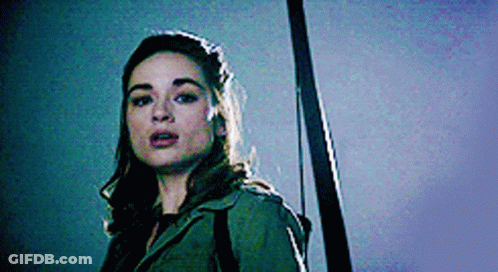A Woman In A Green Jacket Is Holding A Sword . GIF