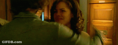 A Woman In A Green Jacket Is Hugging Another Woman In Front Of A Wooden Cabinet GIF