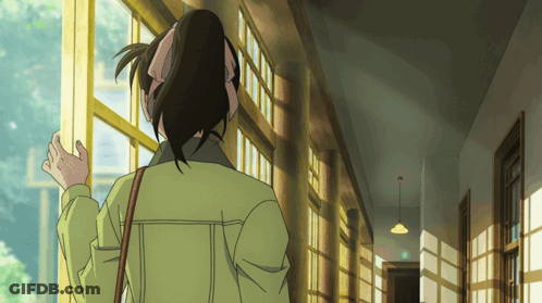 A Woman In A Green Jacket Is Standing In A Hallway Looking Out A Window GIF