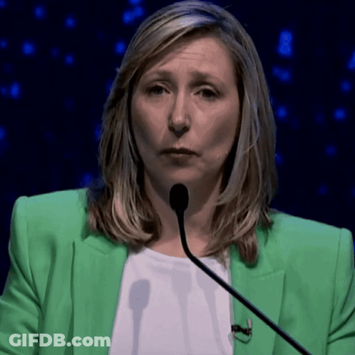 A Woman In A Green Jacket Is Talking Into A Microphone GIF